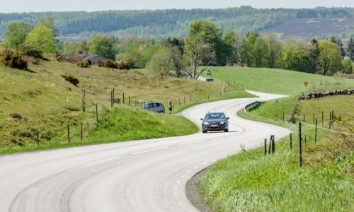 Brosarp: Documentary of Brosarps hills nature area. Car driving the winding road through the scenic landscape. Person standing roadside looking through a scope at car.