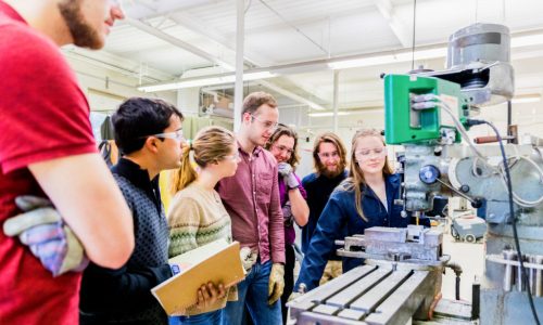 STEM, Education, University - Team of Engineering Students learning how to operate a heavy industrial machinery taught by a senior female student